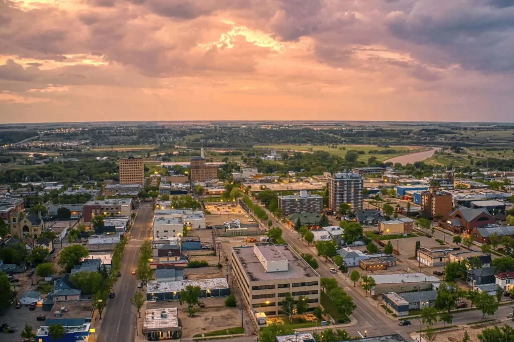 Aerial sunset view of Winkler in Southern Manitoba with homes, roads, and farmland beneath colorful clouds.